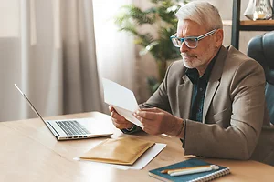 An invoice for payment. Attentive senior man looking at bank statement, high taxes. Check for payment of money.
