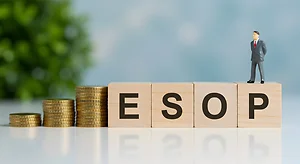 Conceptual Image of Gold Coins and Wooden Blocks Forming ESOP with Miniature Man in Business Setting