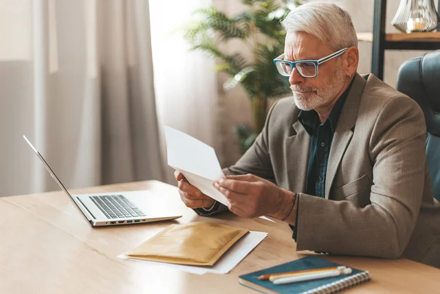 An invoice for payment. Attentive senior man looking at bank statement, high taxes. Check for payment of money.